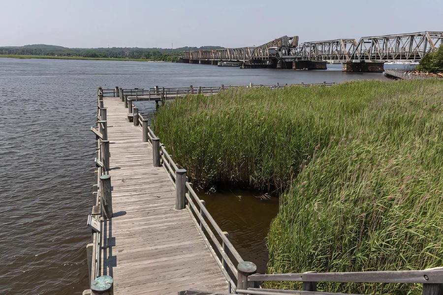Timber fishing pier running through marsh grass on the Connecticut River, railroad bridge in the distance