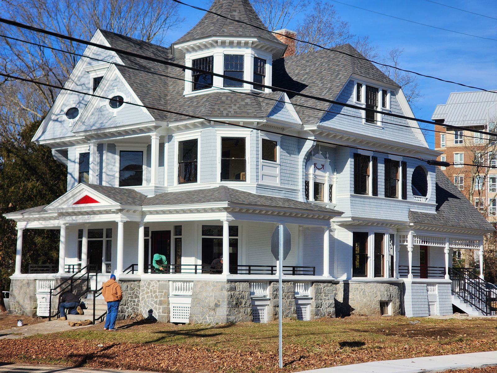Front elevation after restoration: the house repainted white with a new slate-grey roof, the turret and dormers rebuilt, a reconstructed wraparound porch with black steel railings, and the stone foundation repointed