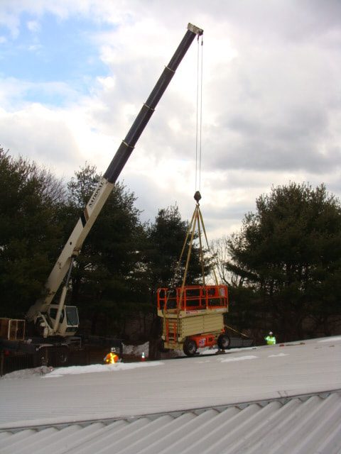 Truck crane hoisting a scissor lift above the basin roof