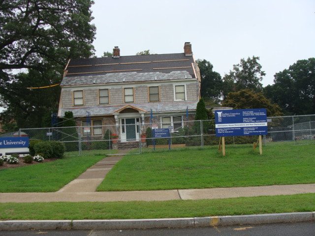 Stone and shingle campus house with SCSU signage and a new roof