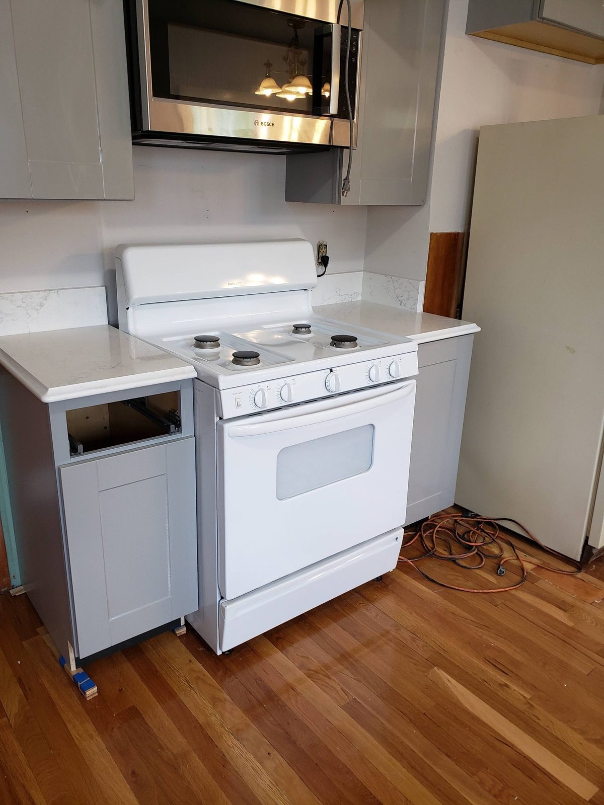 New grey cabinets and white quartz counters and backsplash around the range, with a stainless over-range microwave