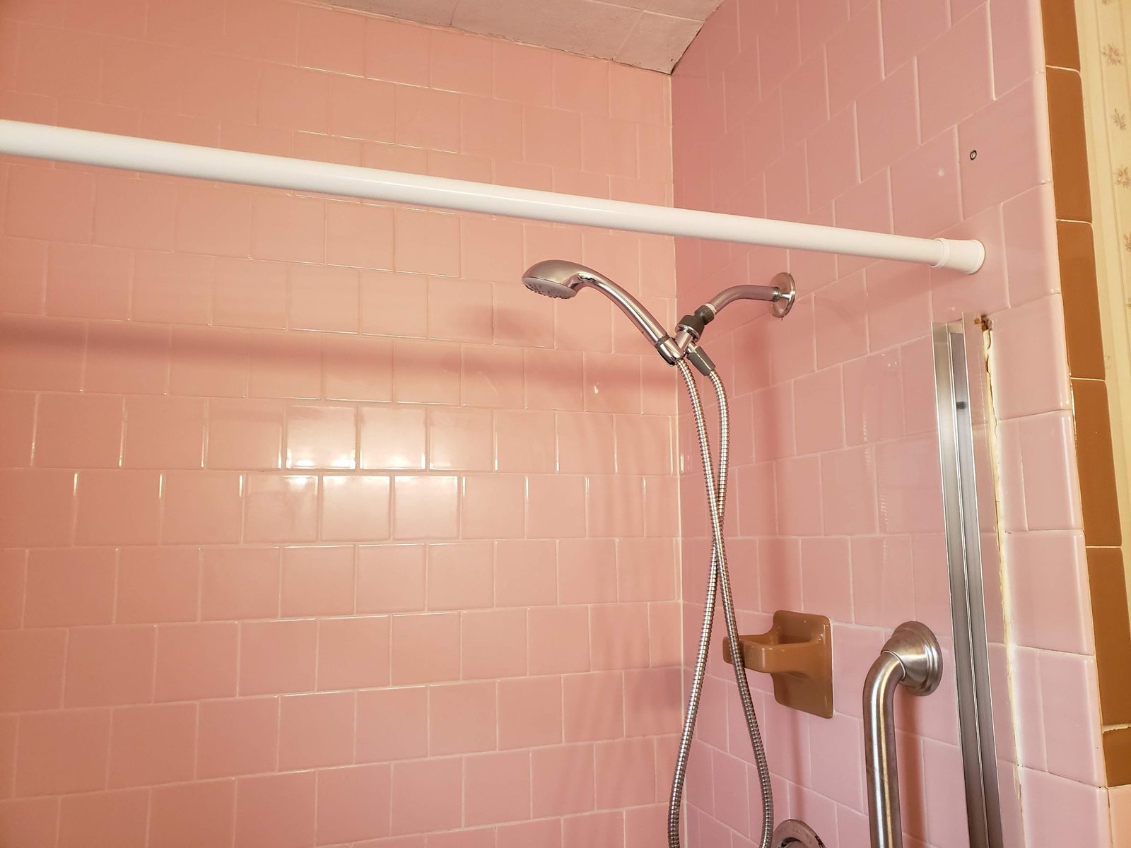 Original pink tile tub surround with a handheld shower and grab bar