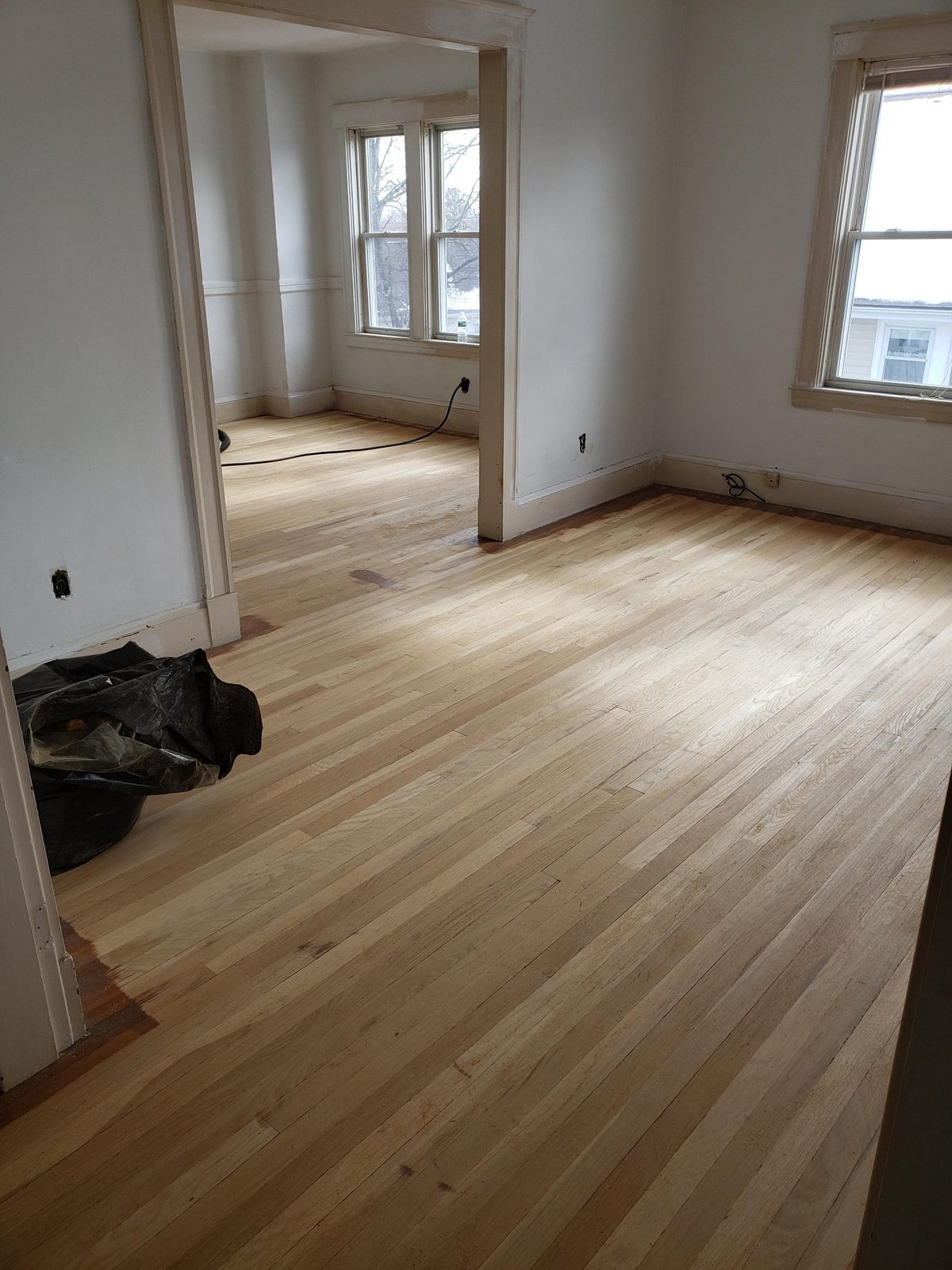 Hardwood floors sanded to bare wood across two rooms, with the walls repainted
