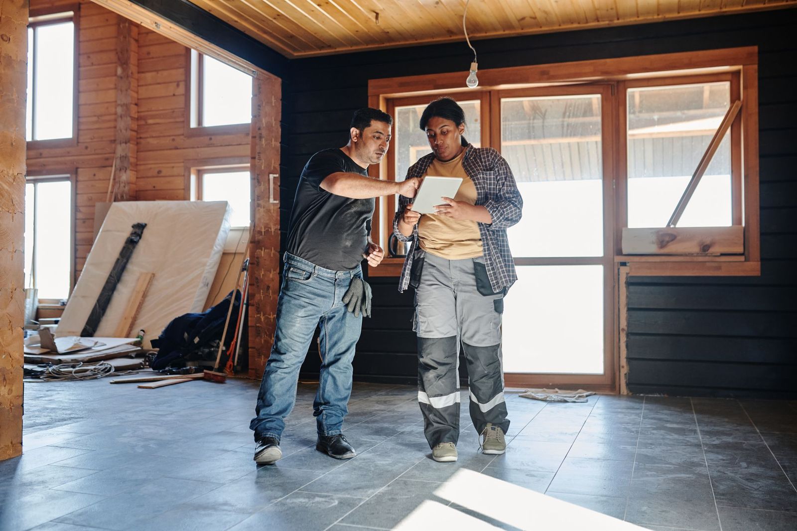 Two tradespeople inside a house under renovation reviewing plans on a digital tablet