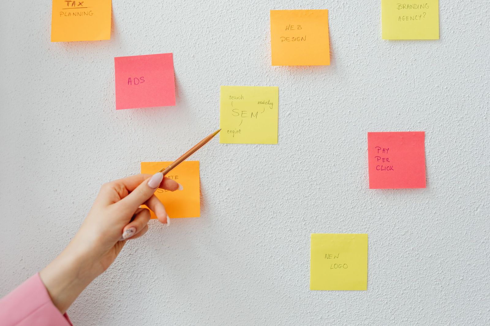 Hand pointing to handwritten tasks on a wall of sticky notes during a planning session